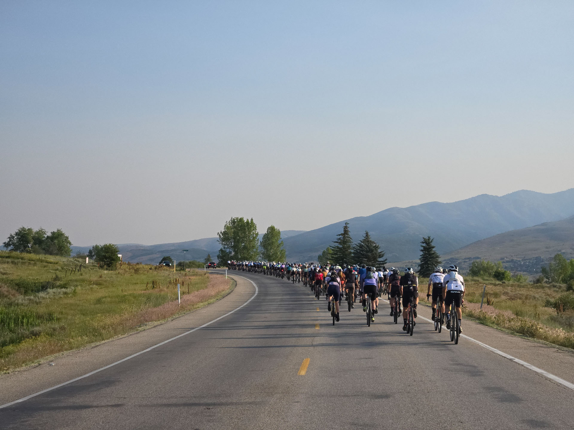 A few hundred Grodeo riders in formation on an empty highway, hazy Wasatch mountains ahead