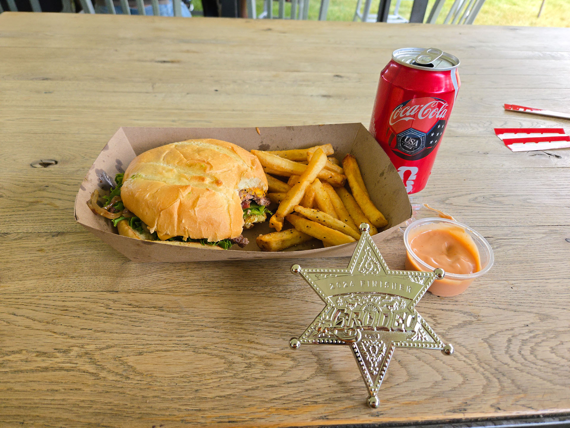 Grodeo finisher's sheriff-star medal next to a burger, fries, and a Coke at the finish