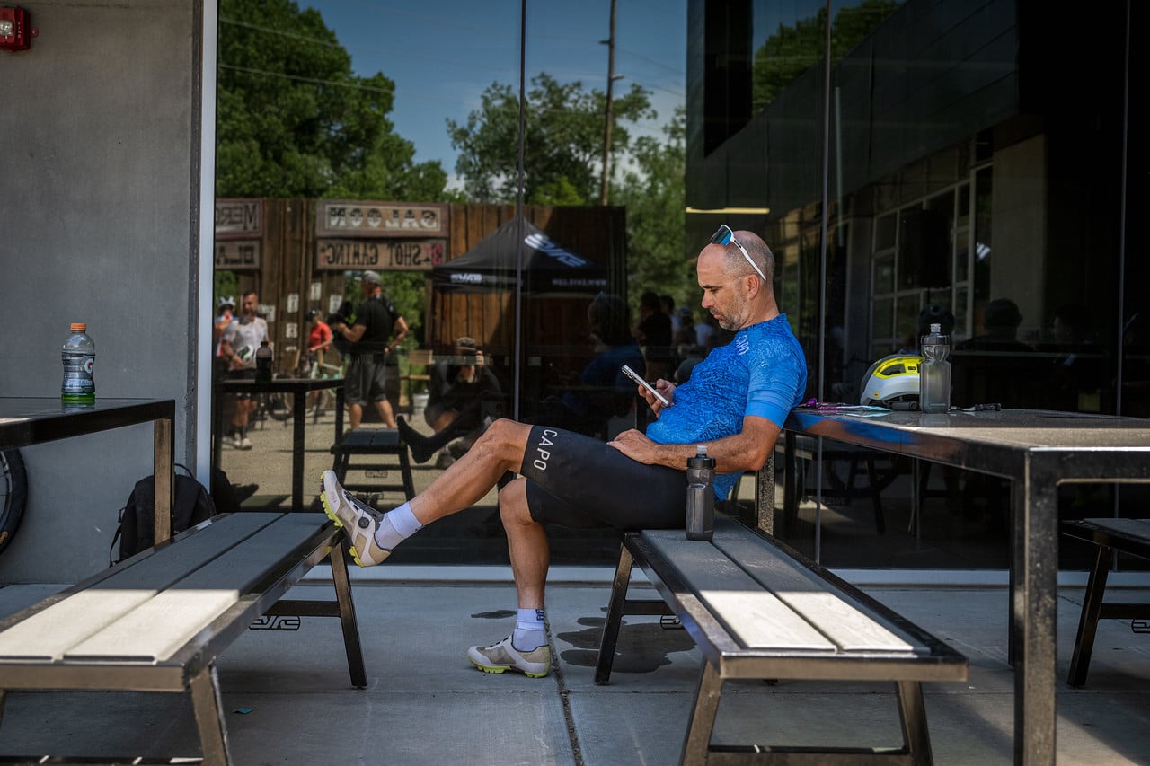Tamas sitting on a bench outside the ENVE showroom, phone in hand, waiting after finishing the Grodeo two hours ahead of the rest of the crew